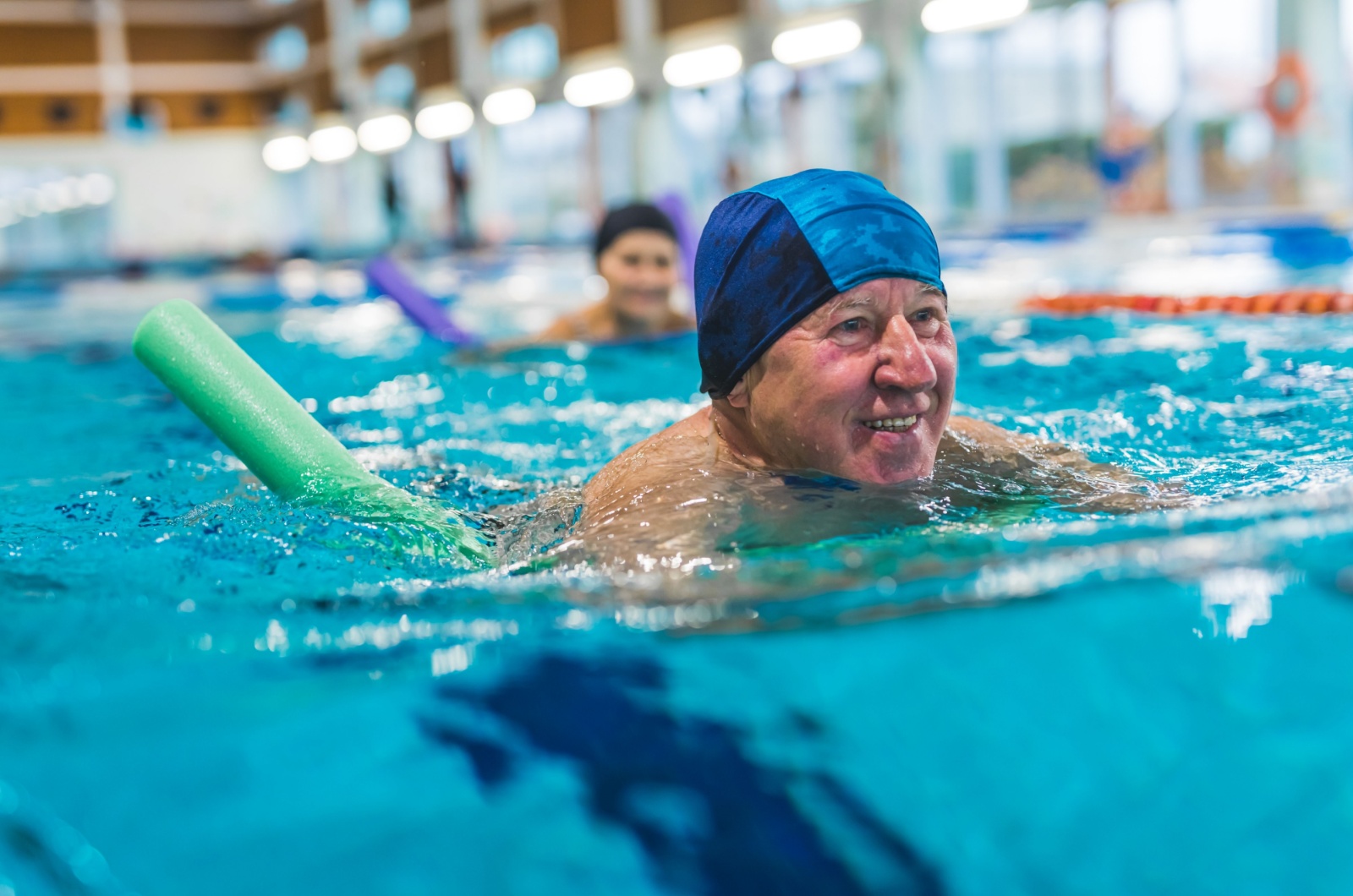 A smiling older adult swimming in a senior living community pool.