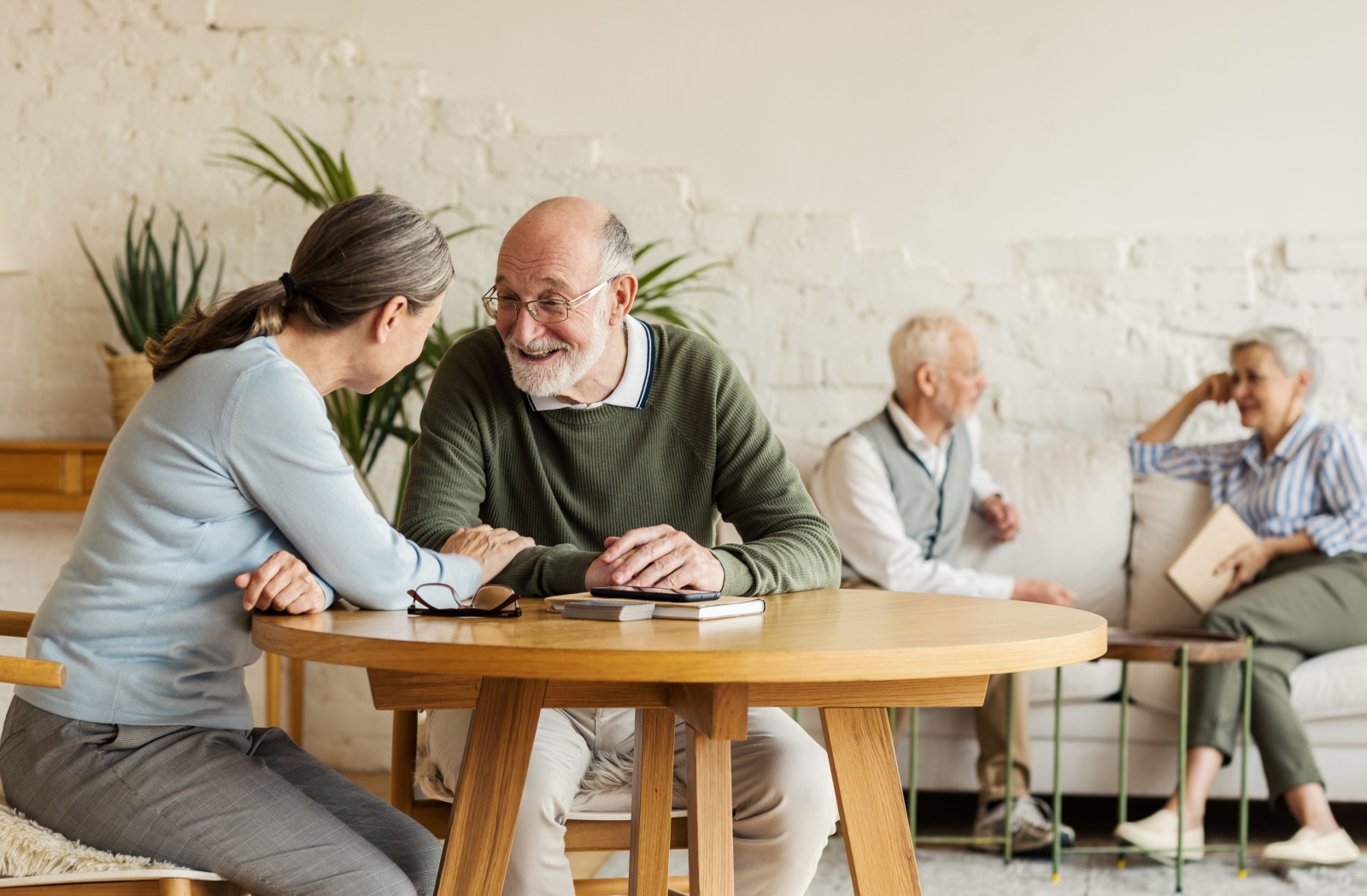 A senior woman and a senior man talking at a round table, with 2 other seniors on the background talking
