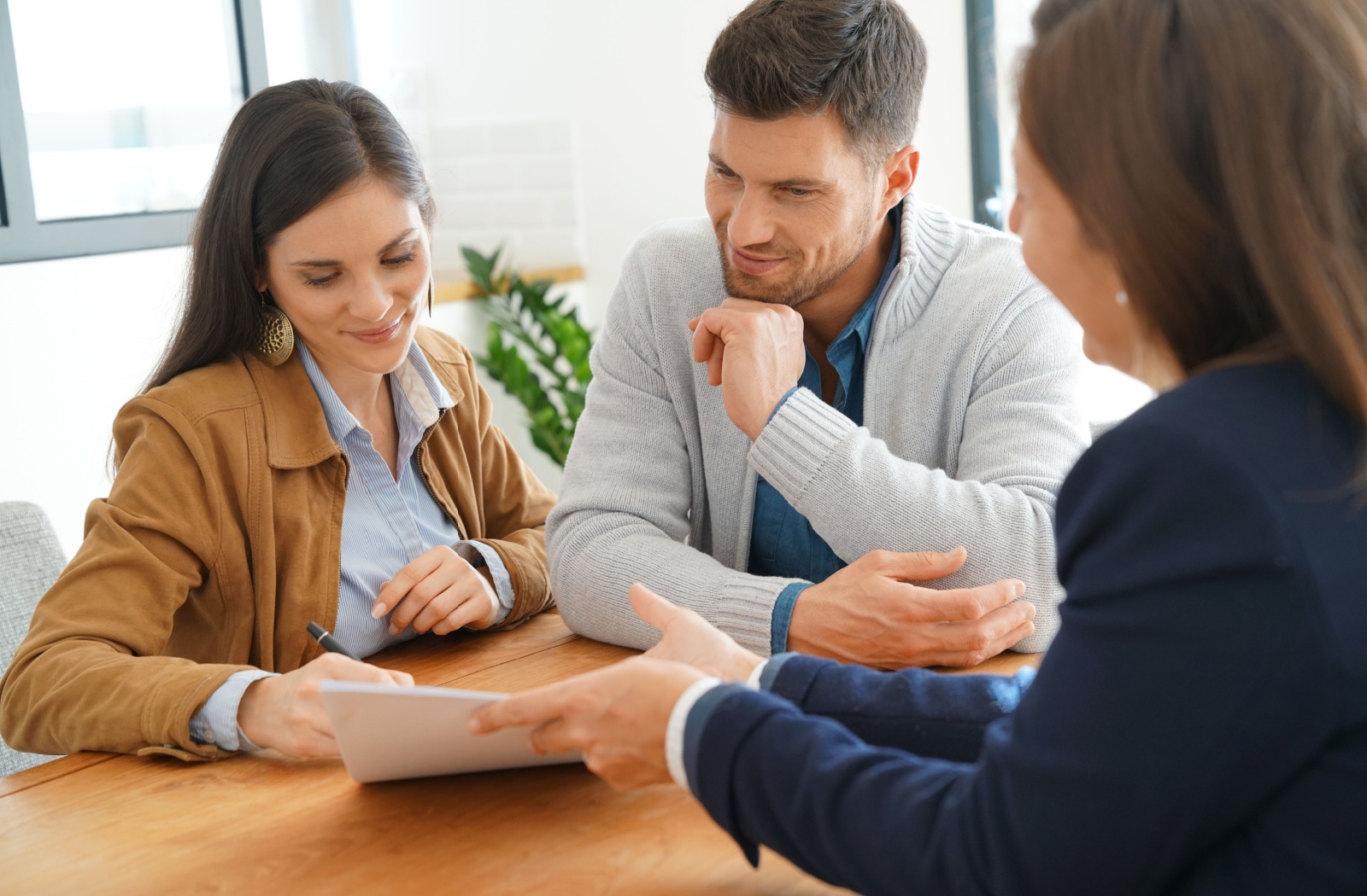 A young couple and attorney sitting at a table and looking at a document that the attorney is showing them
