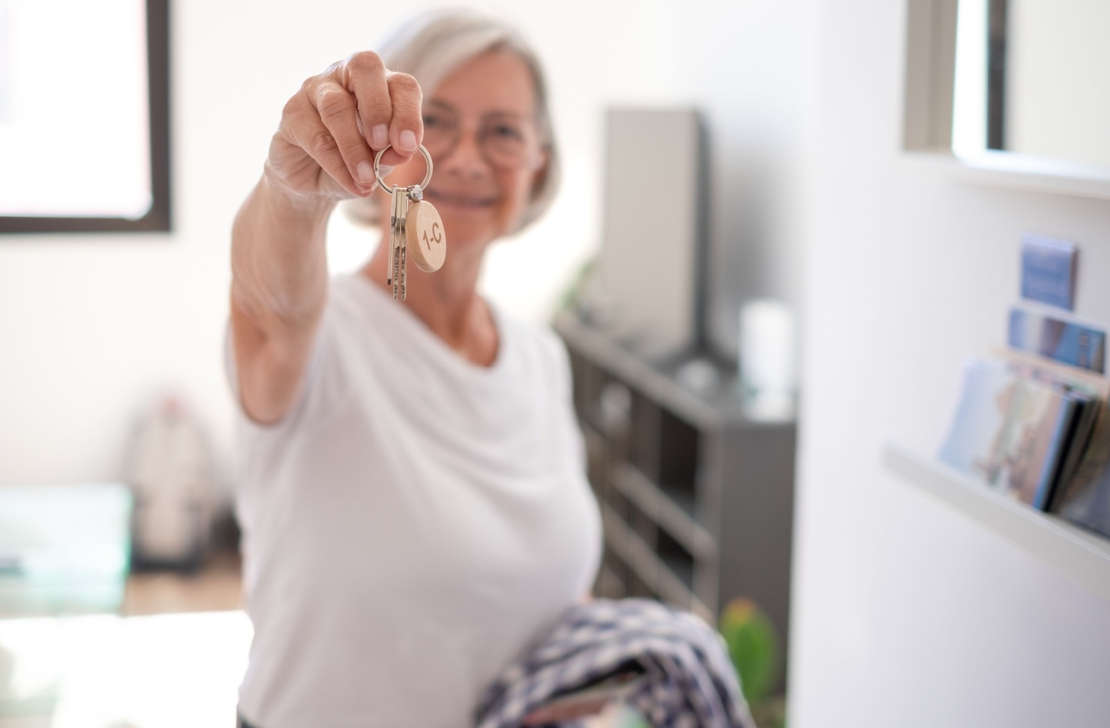 An older adult smiling and holding up a new set of keys for their new, downsized home.