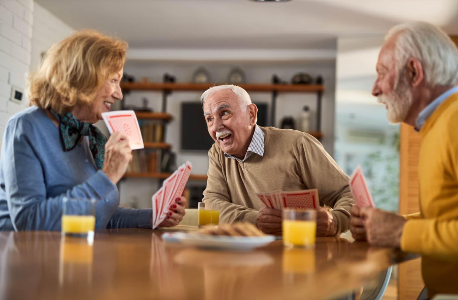 3 older adults sitting around a table playing cards and smiling at breakfast in an assisted living community.