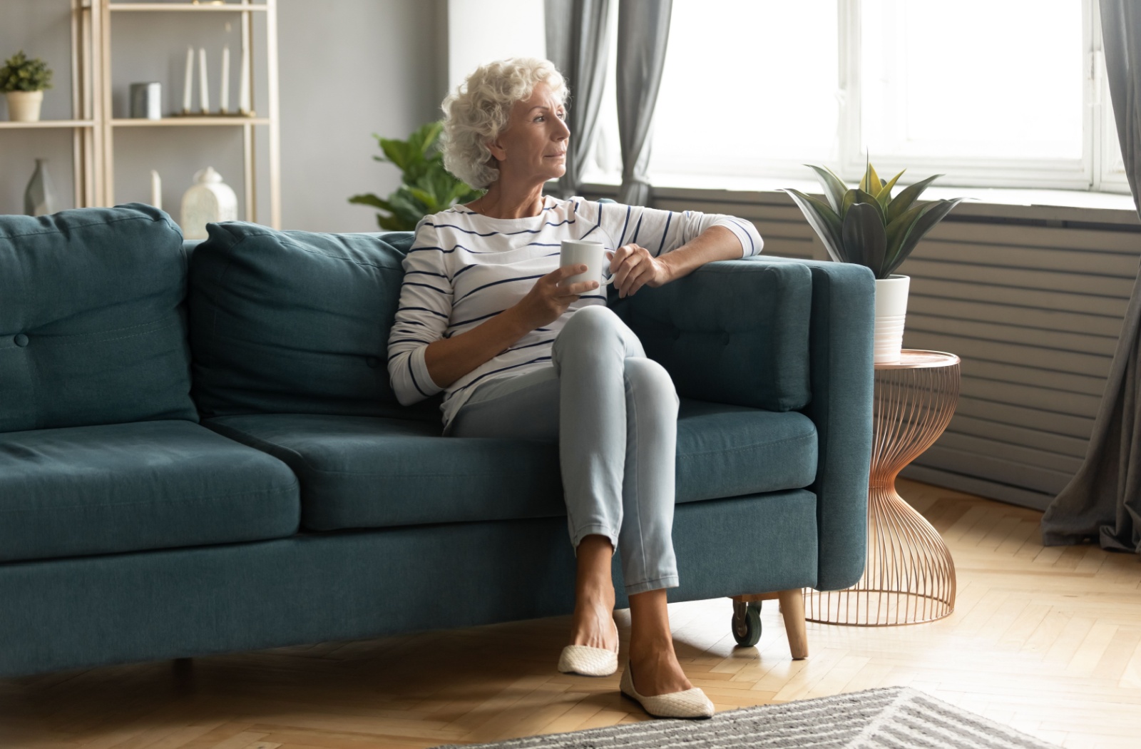 An older adult relaxing on the couch with a cup of tea in their new assisted living apartment.