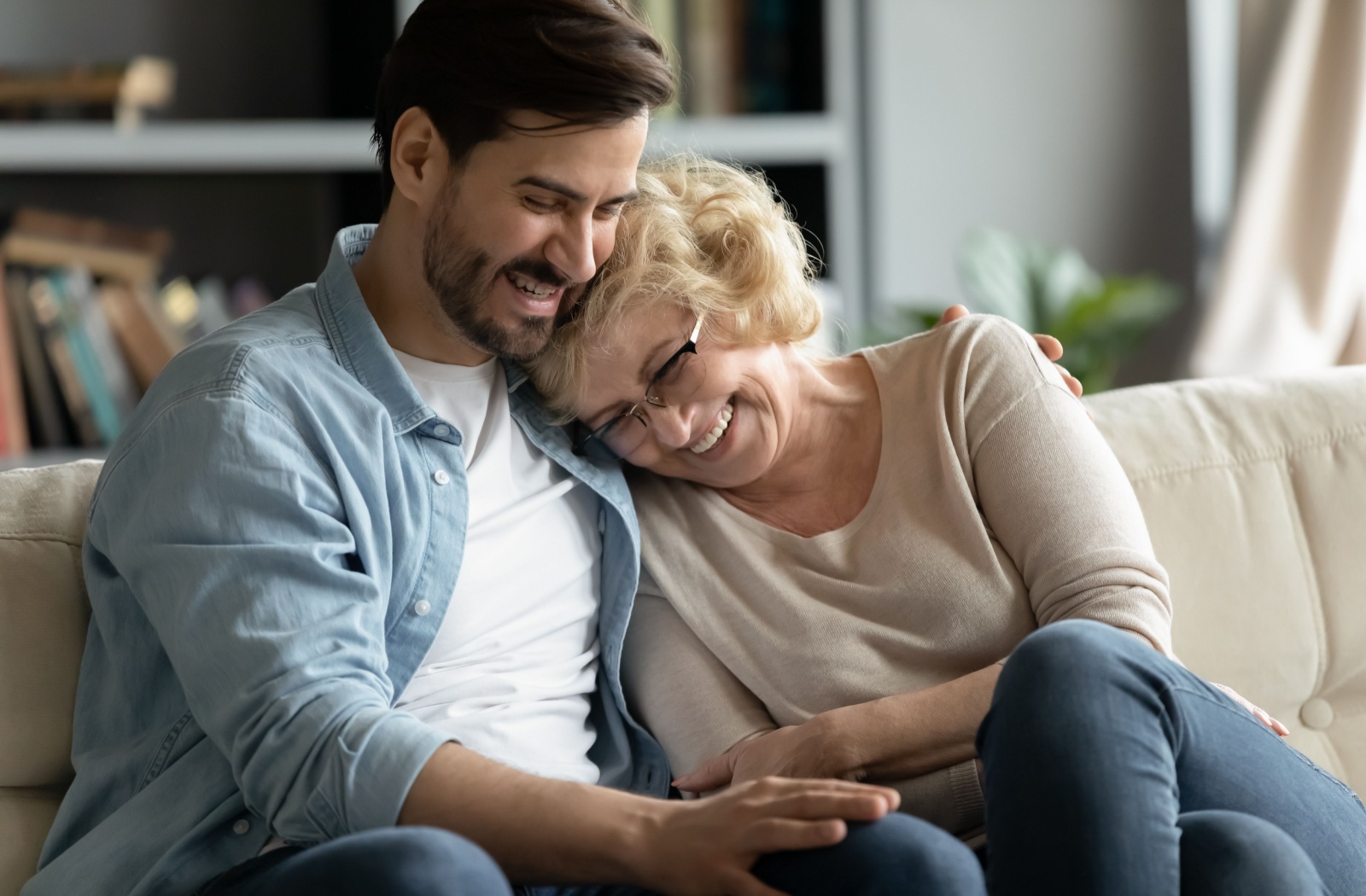 An adult child hugging their older parent on the couch during a visit to their senior living community.