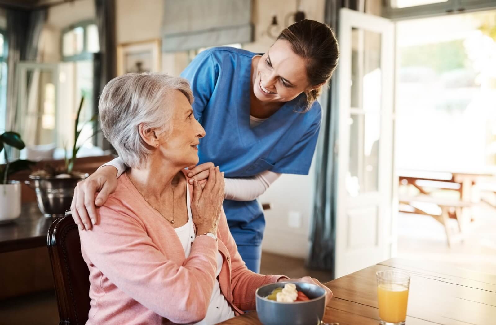 A caregiver checks on a memory care resident as they eat a healthy breakfast in their community.
