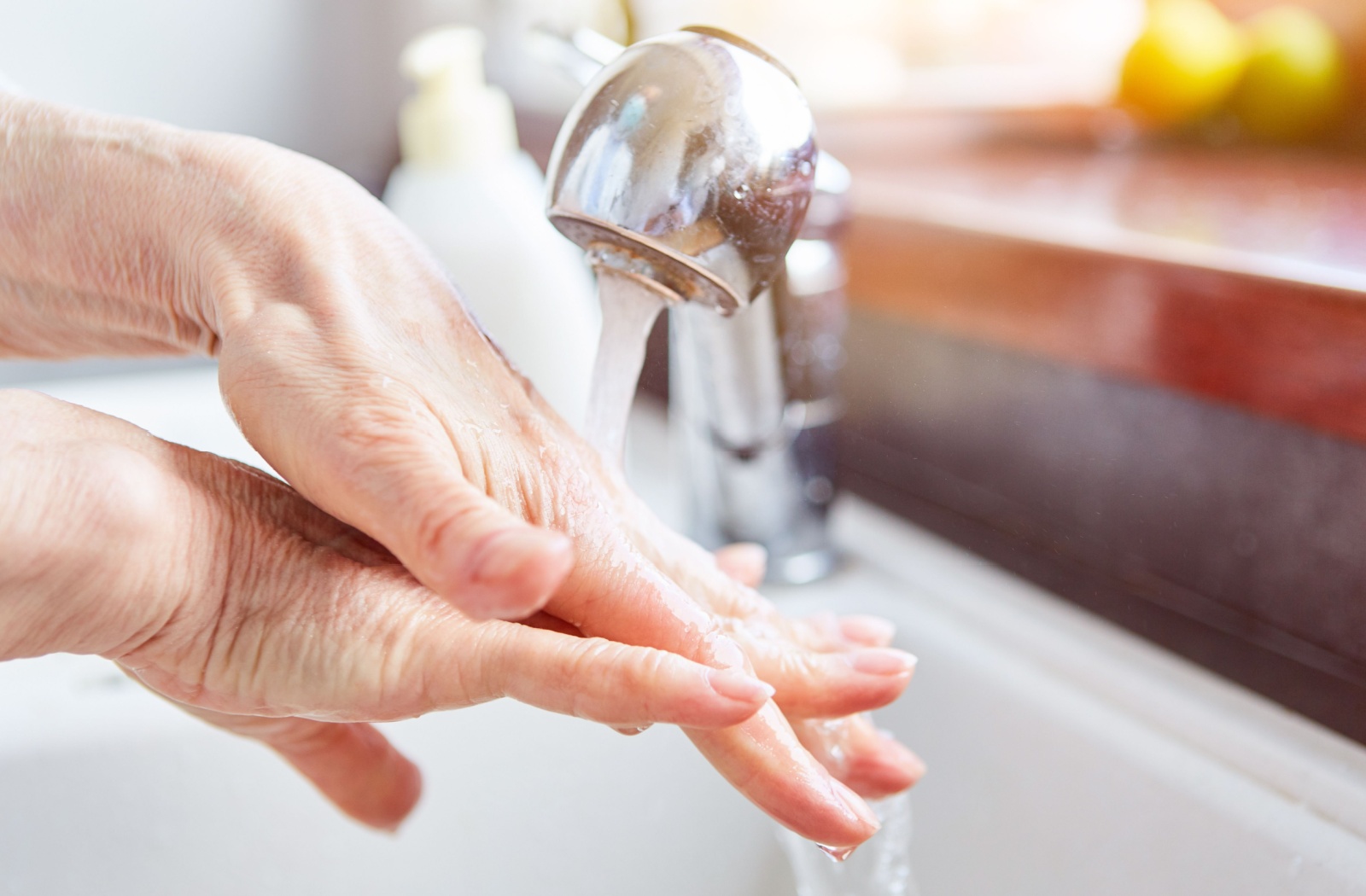 A close-up image of an older adult washing their hands in their kitchen sink