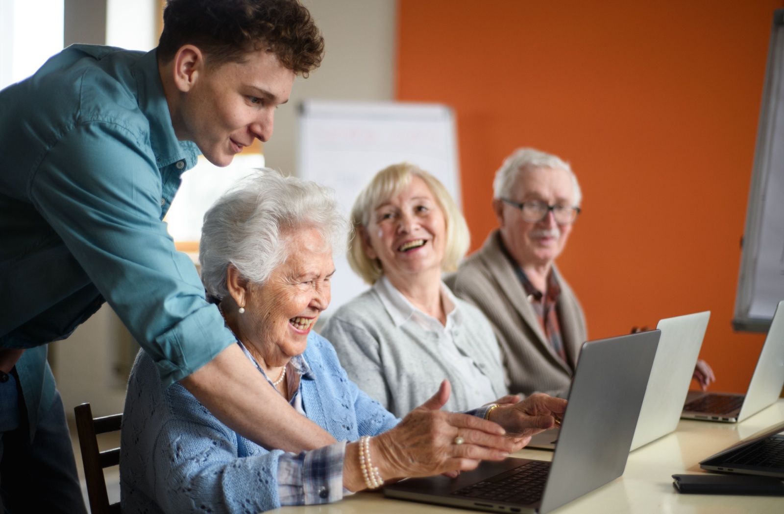 A young man shows a smiling group of seniors how to use their laptops.
