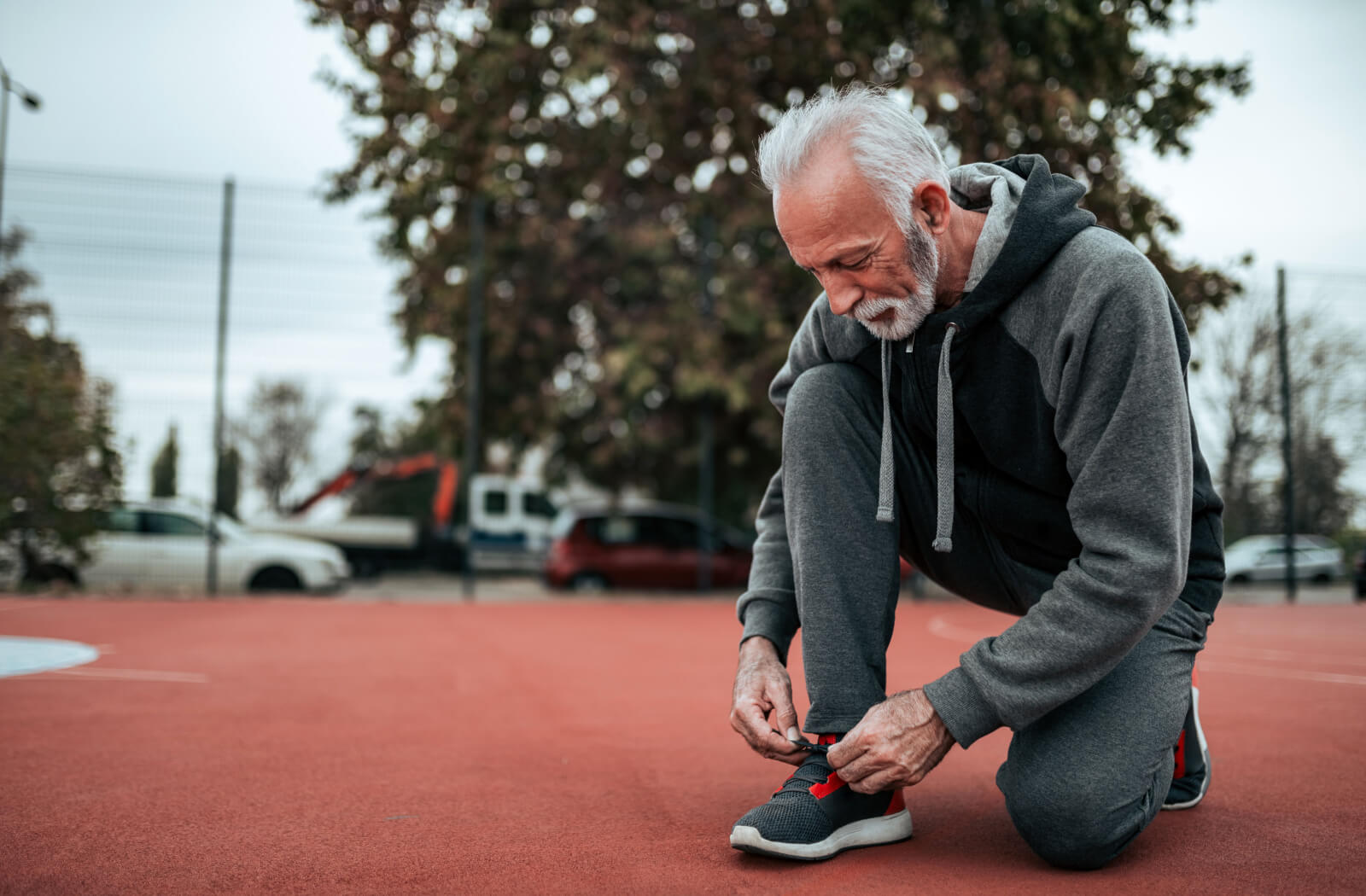 An older adult wearing athletic gear on a tennis court smiling while tying up his new shoes.