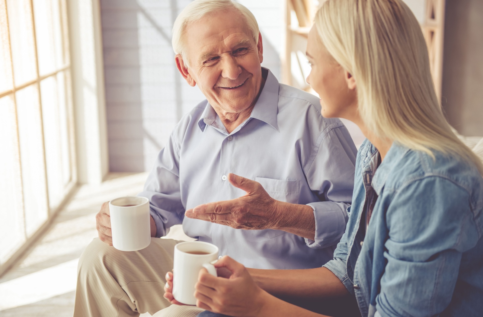 A senior and his adult child chatting and laughing together while they enjoy a tea.