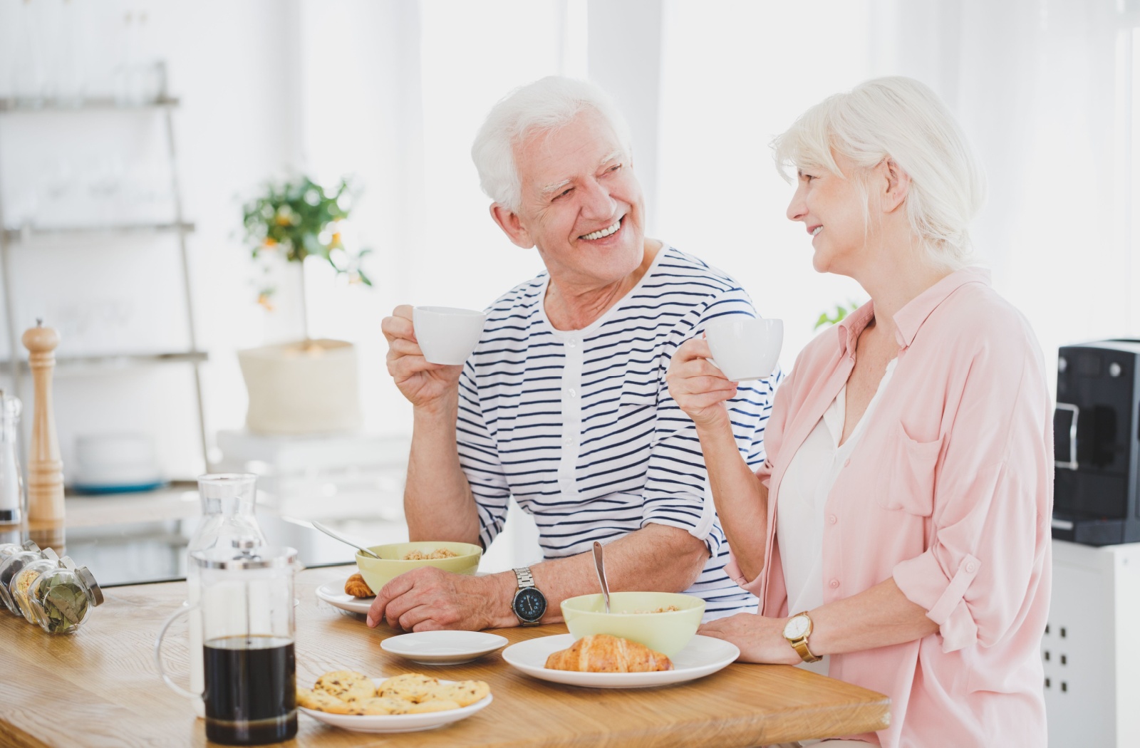 An older adult couple in assisted living eating together in a brightly lit dining area.
