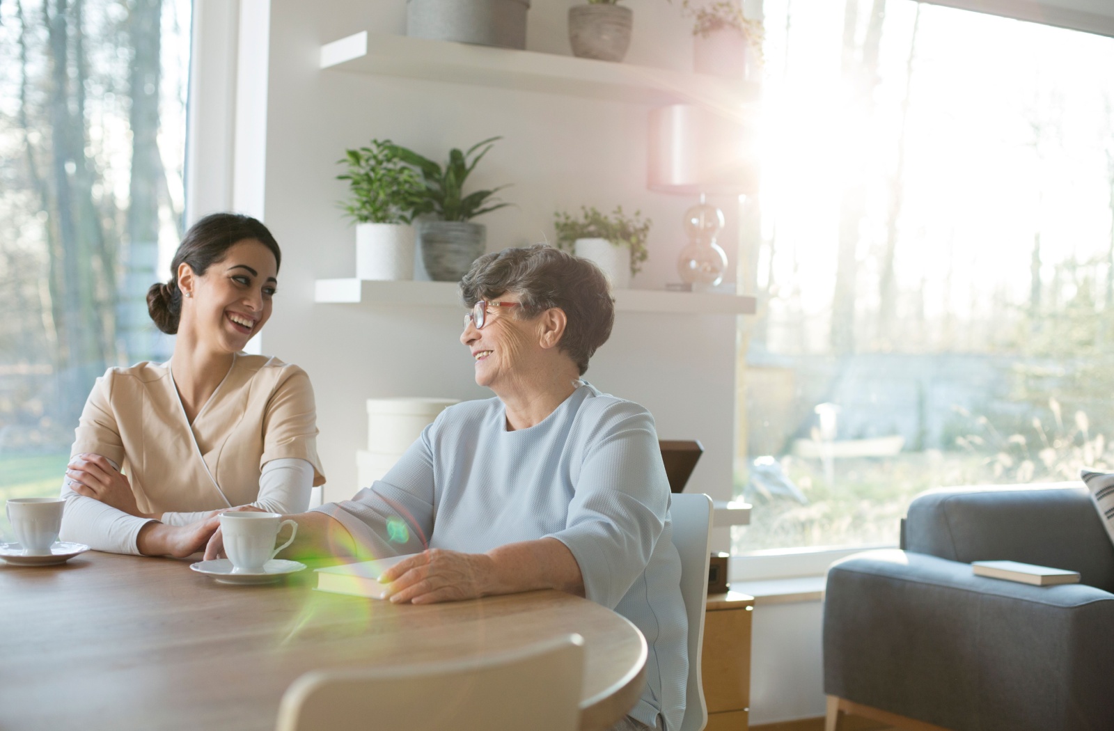 A adult child laughing and having tea while visiting their elderly parent with dementia.