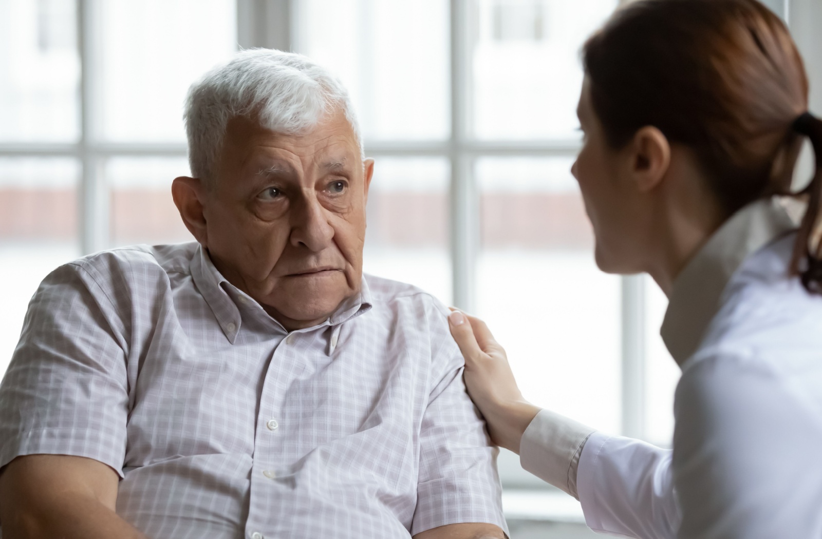 An adult child putting their hand on their elderly parent's shoulder to comfort them.
