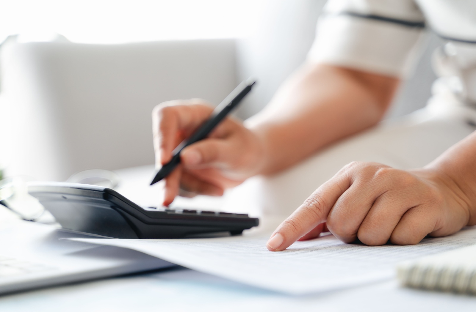 Close-up of a person typing on a calculator and pointing at a line on a paper document