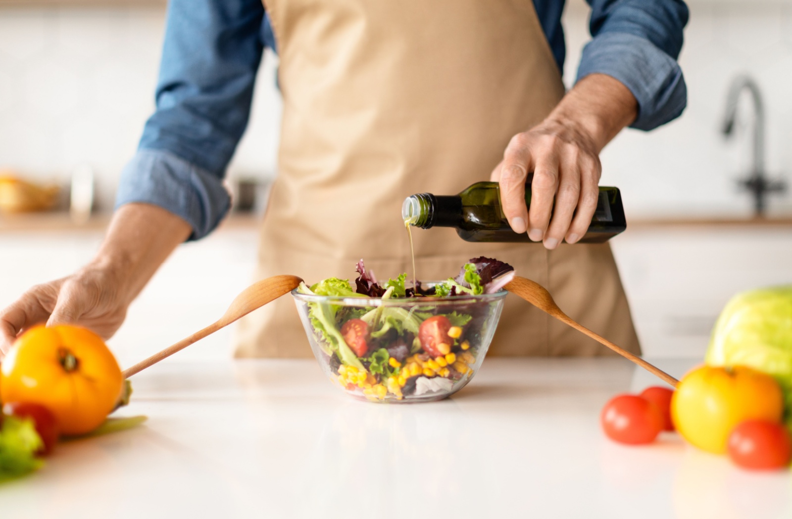 A close-up image of an older adult pouring olive oil over a bowl of salad.