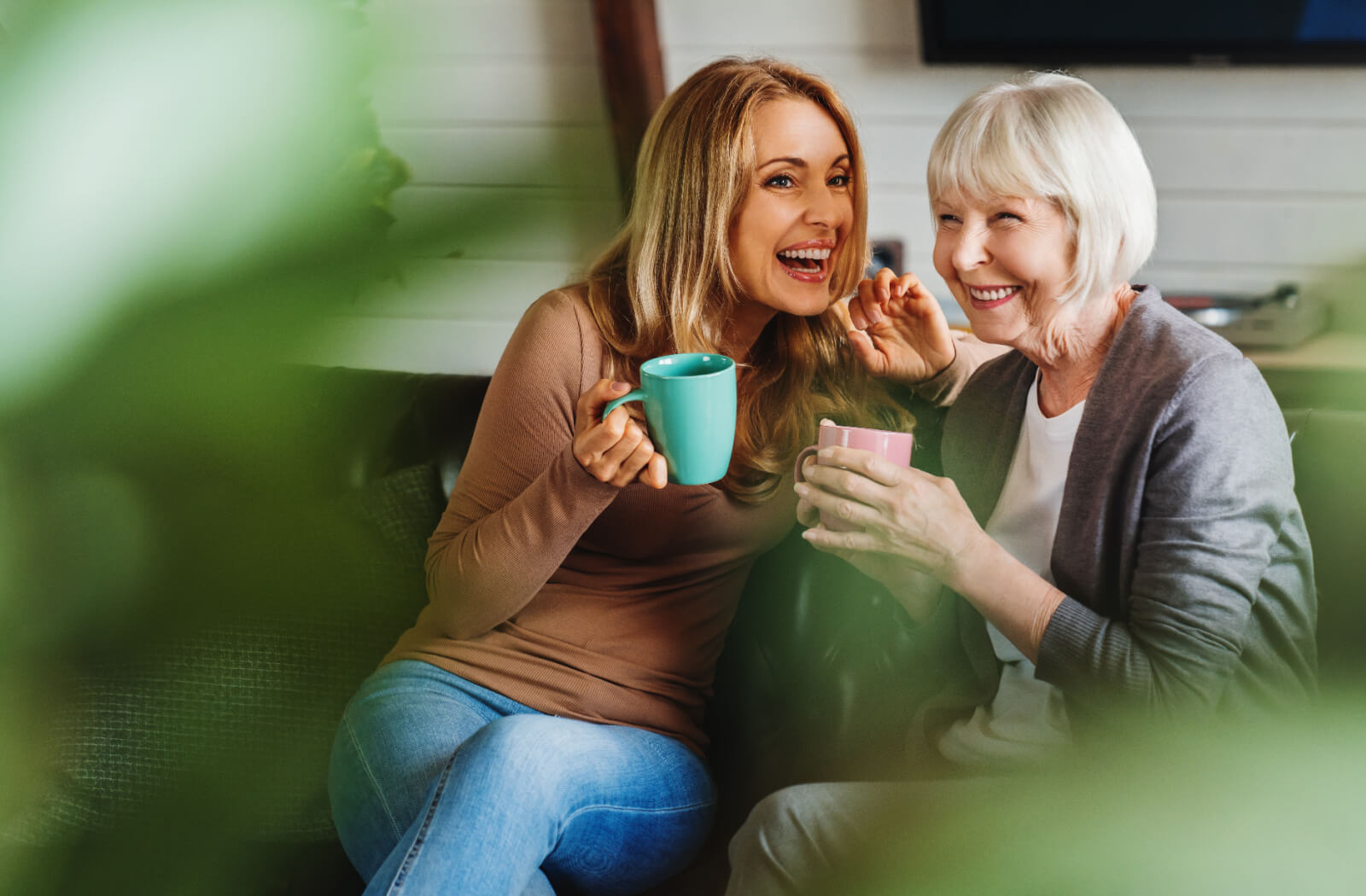 An older adult and their adult child drinking coffee and laughing together during a visit in senior living.